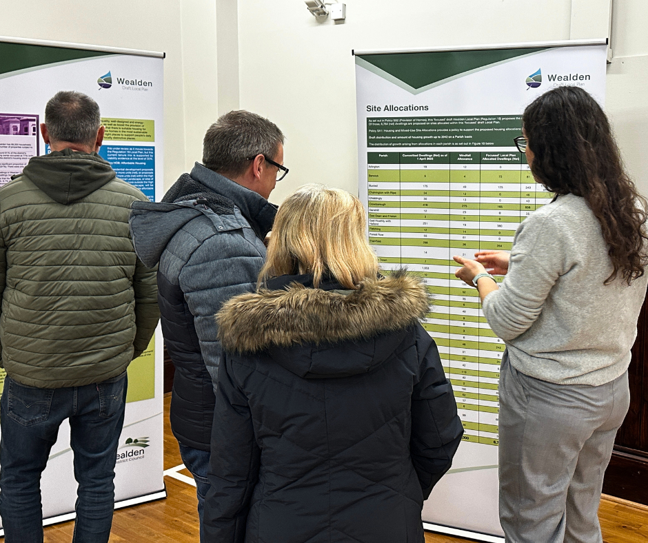 Group of people gathered around a pull up banner discussing the Draft Local Plan.