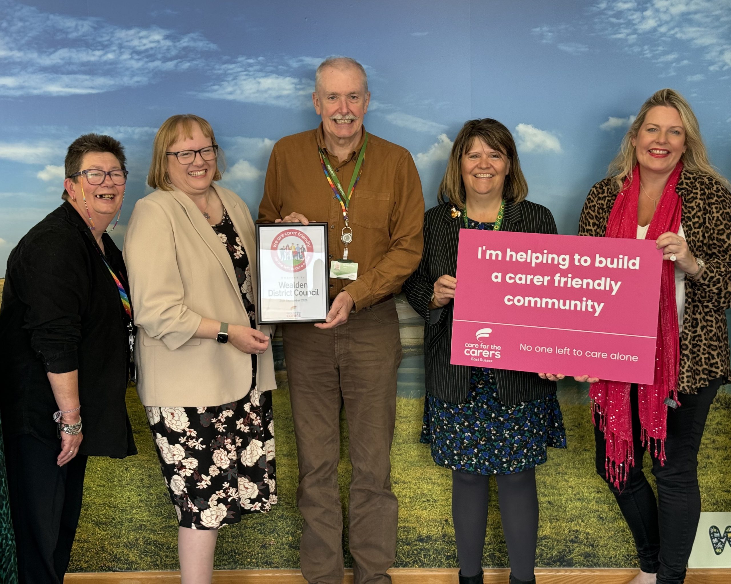 A group of carers holding a board with text 'I'm helping to build a carer friendly community'