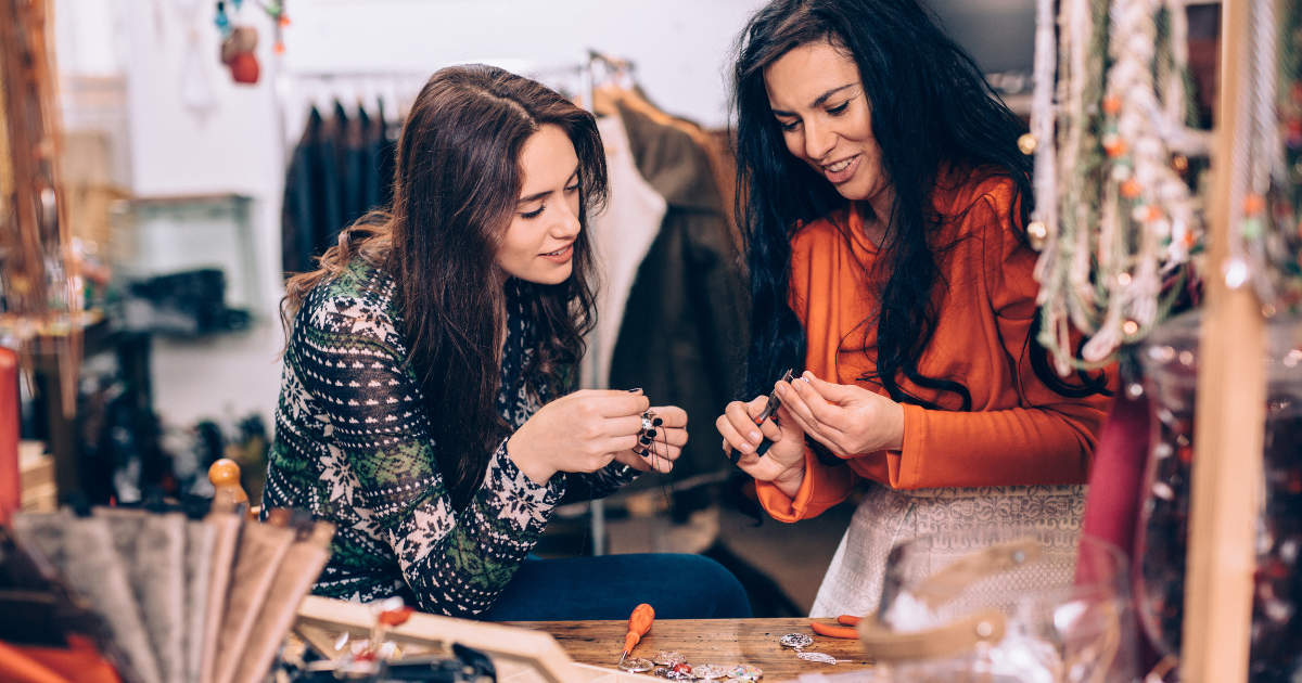 two women standing next to each other crafting. the lady on the left is watching the other person whilst they sew