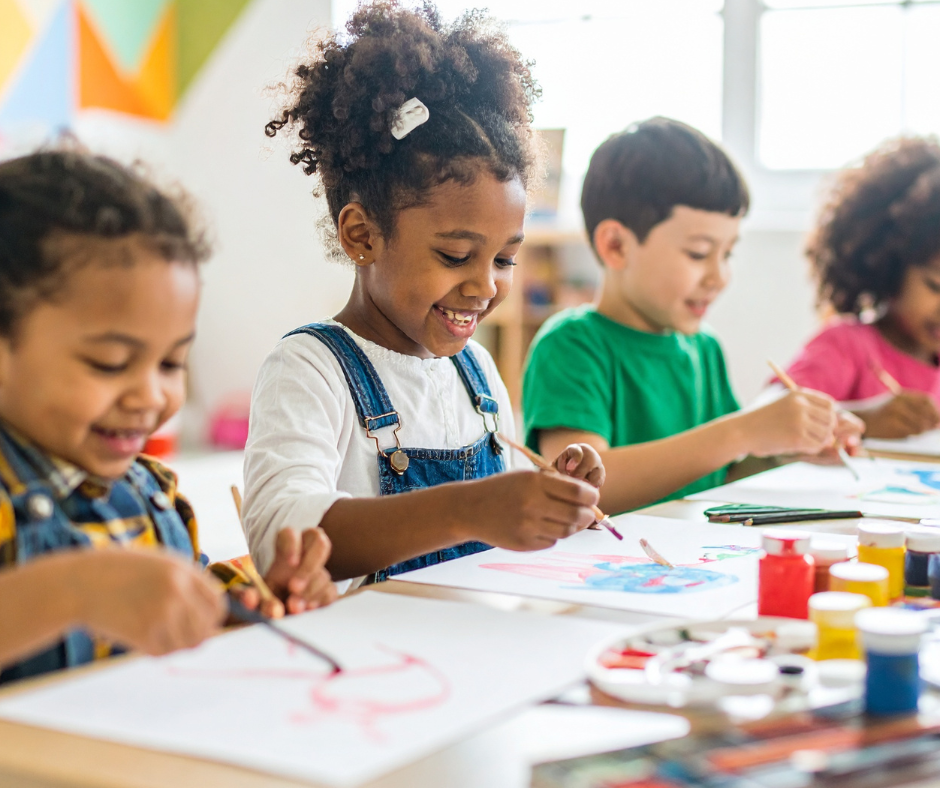 children sat at a table painting on pieces of paper. the children are smiling